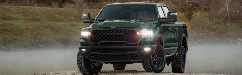 Green RAM pickup truck driving on a rugged dirt road.